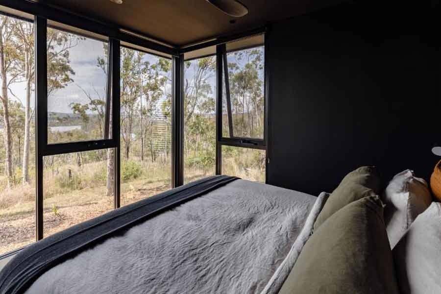 Bedroom corner with a row of open awning windows looking onto trees and grass.
