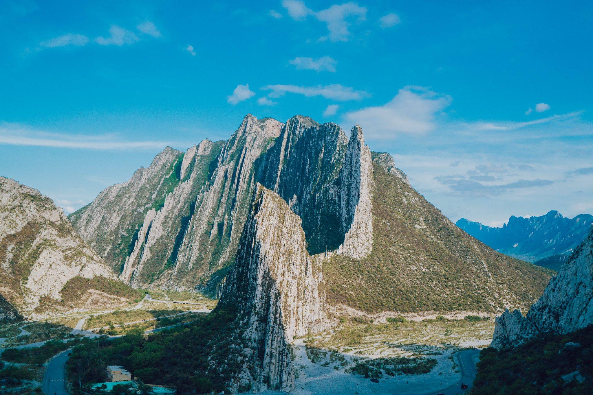 Steep pale rock peaks rising over a green valley and a dry riverbed.