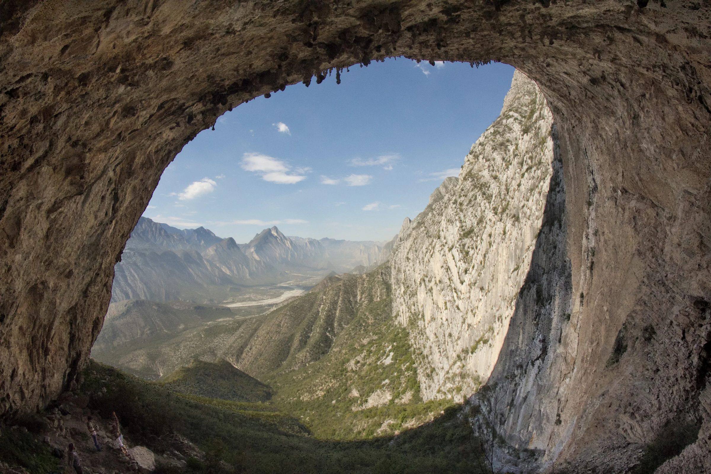 Green valley and limestone cliffs seen through the mouth of a rock overhang.